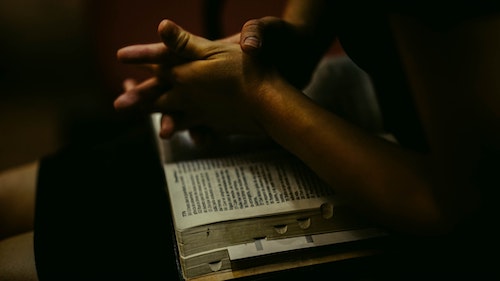 hands folded on top of open bible